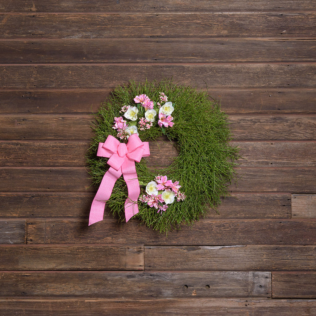 Decorative wreath with flowers and a pink bow on a wooden background