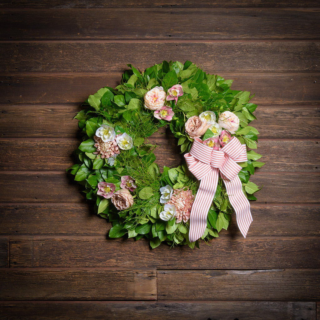 Decorative wreath with flowers and a pink bow on a wooden background