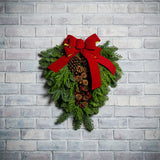 Christmas Swag made with fir cedar juniper pine cone glittery branches silver balls and red bow on white brick background