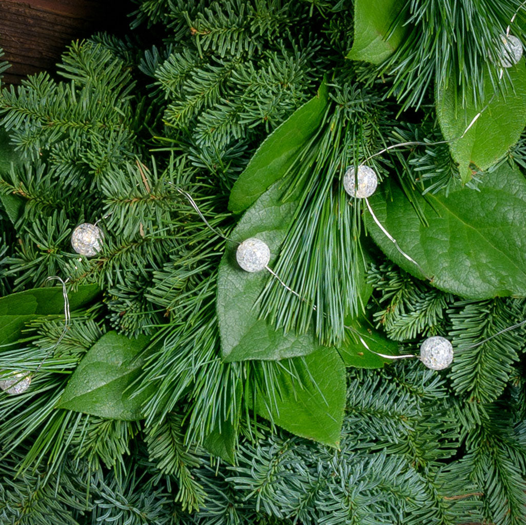 White, globe shaped, cracked glass effect battery operated lights on a evergreen wreath close up