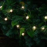 White, globe shaped, cracked glass effect battery operated lights on a evergreen wreath close up illuminated