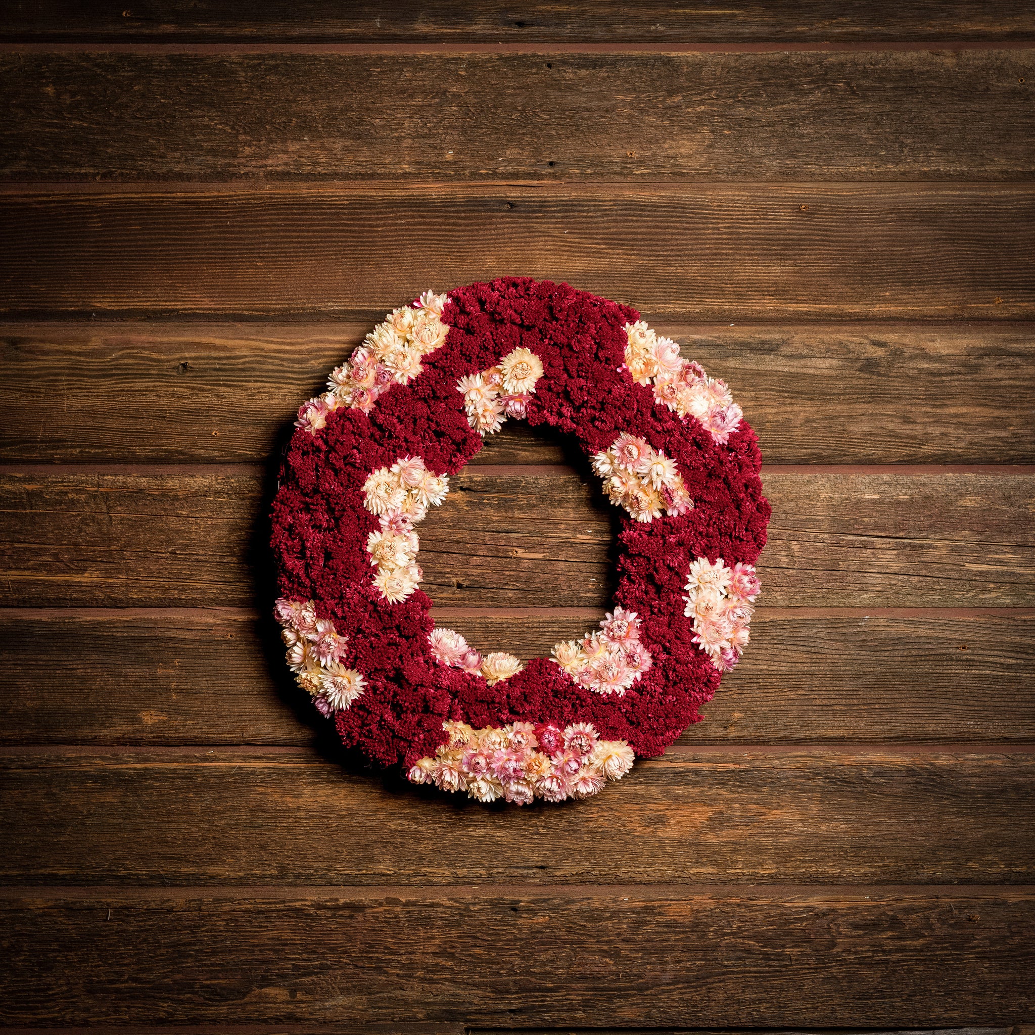 Wreath made of Burgundy-colored ceosia (also called coxcomb) and pale pink strawflowers on a dark wooden background.