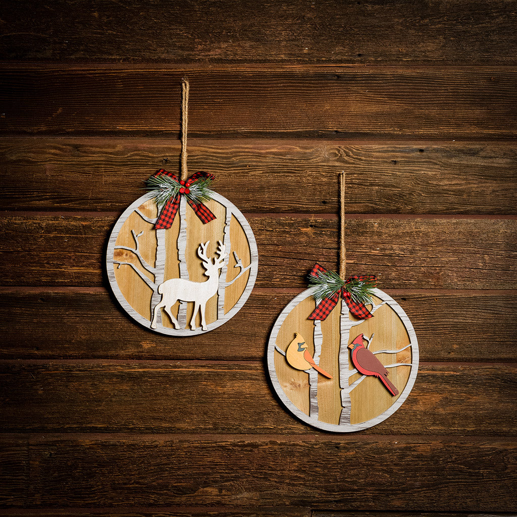 Set of 2 10 inch circular signs with deer and birds hanging on a dark wooden background.