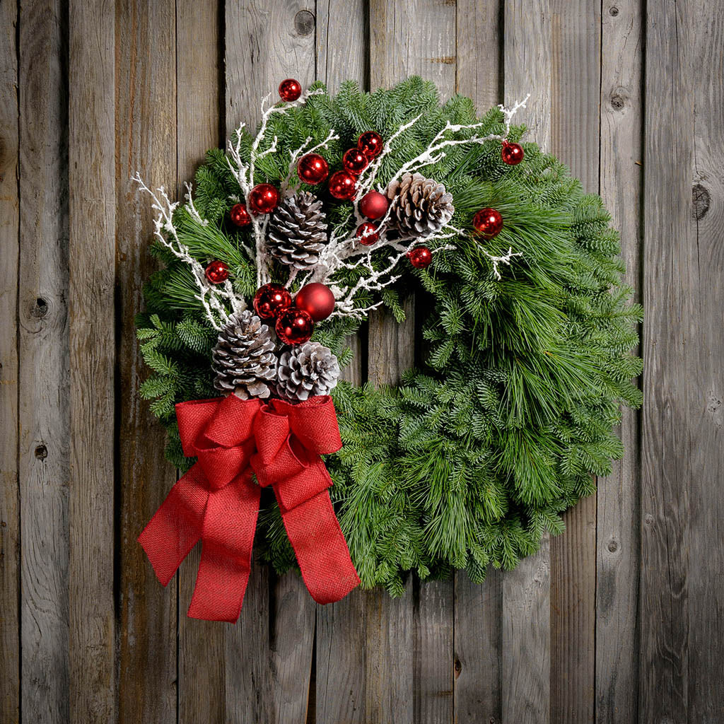 Christmas wreath with pine cones, snow-covered branches, red balls and a red burlap bow on a wooden plank background