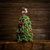 A Table top tree made of noble fir with 8 Australian Cones, 12 red berry clusters, 6 small Tartan bows, and a wooden reindeer with a wood background. 