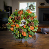 Holiday wreath made of noble fir, cedar, and pine with bay and magnolia leaves, ponderosa pine cones, and Australian pine cones on a wreath stand on a wooden table