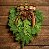Christmas Swag made with fir cedar juniper pine cones and gold and burgundy bow on a wood background.