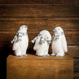 Set of 3 white penguins with gray and white scarves standing on a wood table with a dark wooden background.