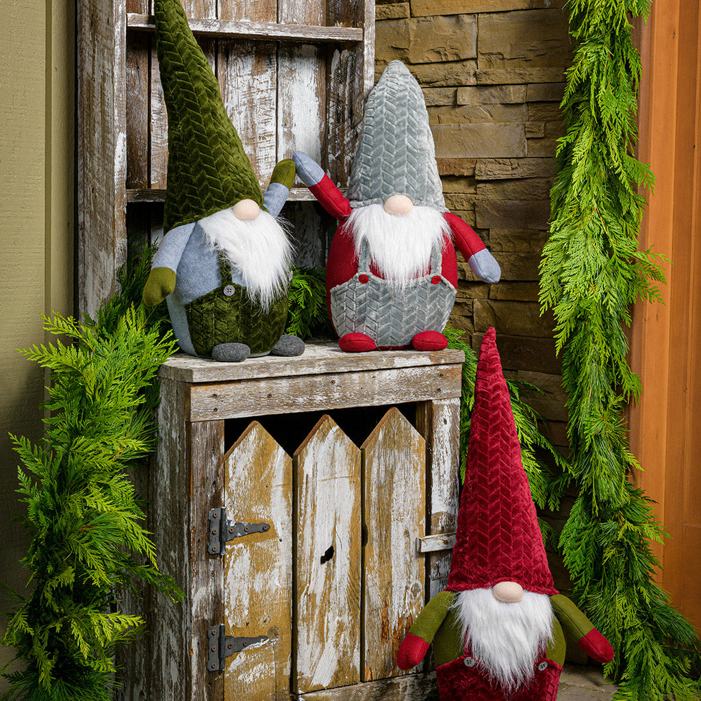 32” Gnomes weighted at the bottom with their noses poking out of tall pointy hats, their fuzzy white beards, and outfits sitting on a wood shelf on a porch.