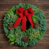 Christmas wreath made of fir, pine, cedar and juniper with pine cones and a gold-backed red velveteen bow
