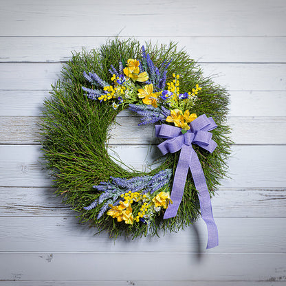 Green wreath with yellow flowers and a purple ribbon on a white wooden background