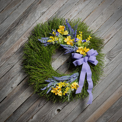 Green wreath with yellow and purple flowers and a purple ribbon on a wooden background