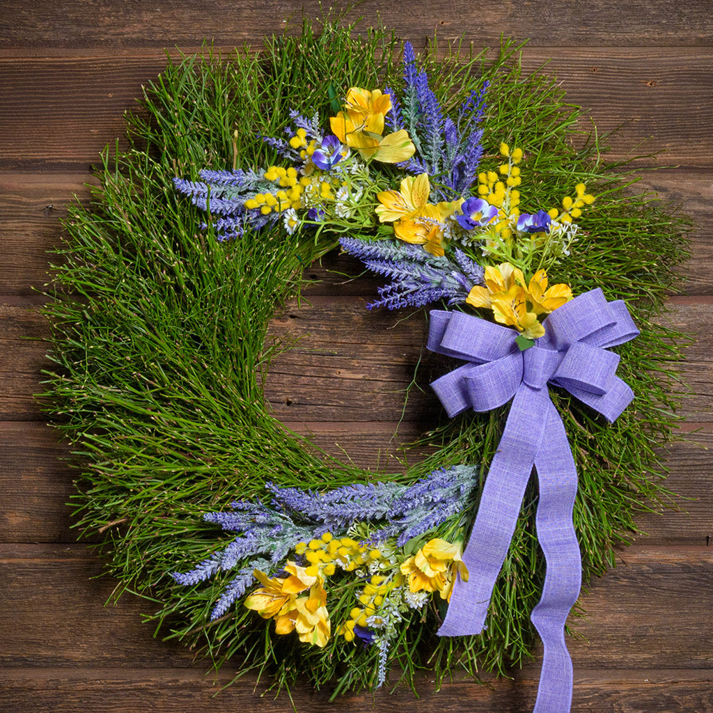 Wreath with greenery, yellow flowers, and a purple ribbon on a wooden background
