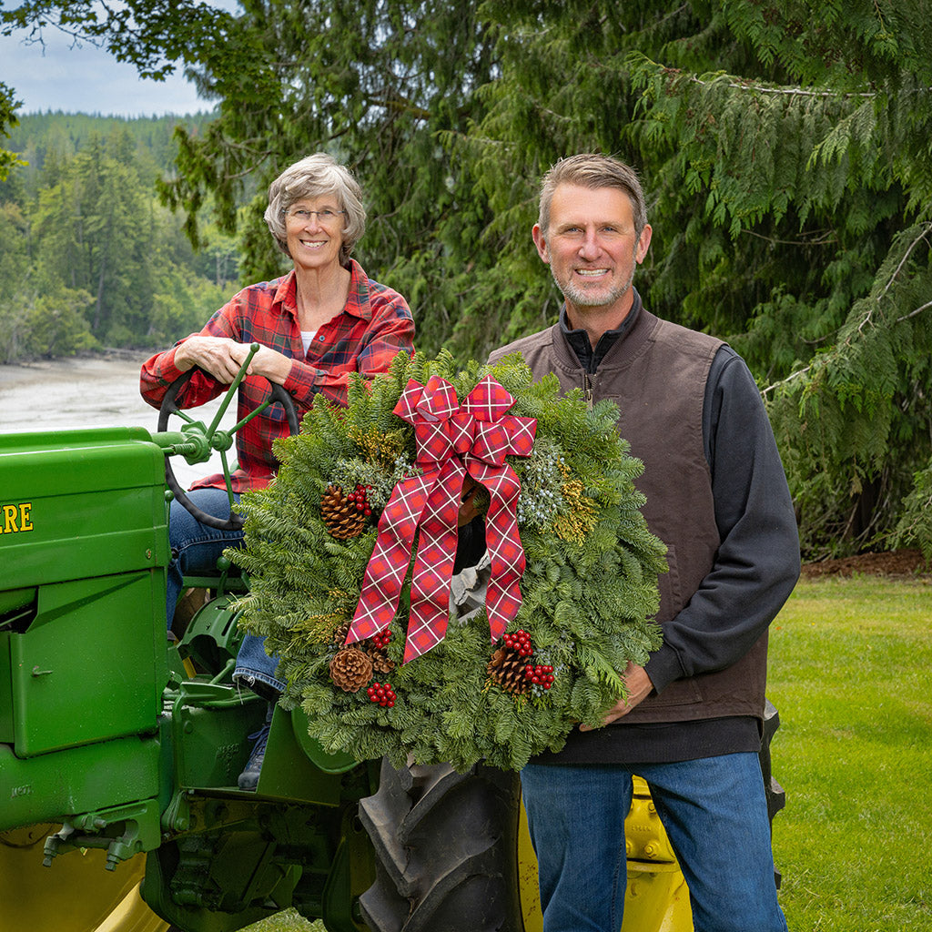 Two people with a large wreath on a green tractor in a forest setting