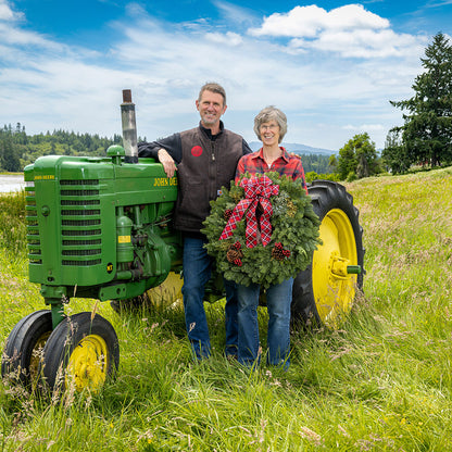 Two people standing next to a green John Deere tractor in a field with a wreath.