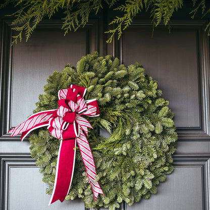 Green Christmas wreath with a red and white bow on a dark door