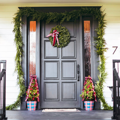 Decorative wreath with a red bow on a gray front door with greenery and potted plants.