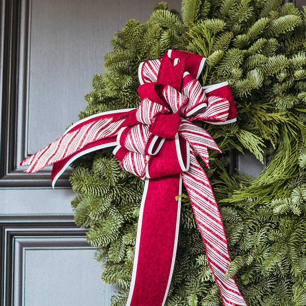 Green wreath with a large red and white striped bow on a gray door.