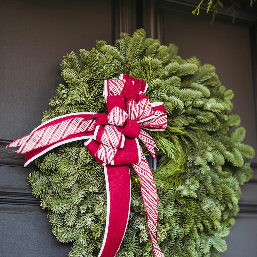 Green Christmas wreath with a red and white bow on a dark surface