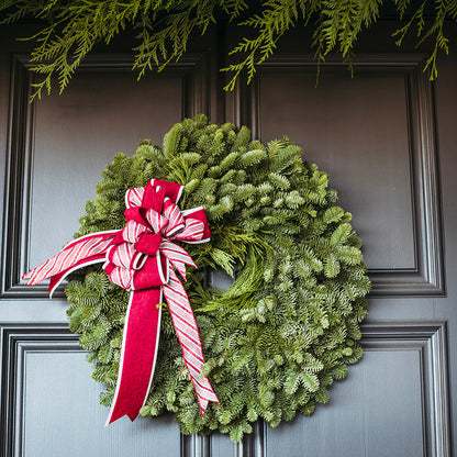 Green Christmas wreath with a red and white bow on a dark door
