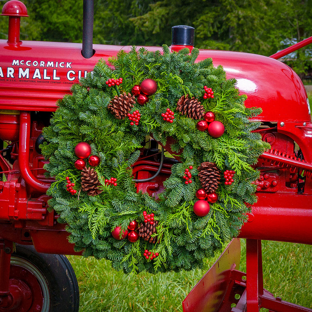 An evergreen wreath of noble fir and cedar with natural pinecones, faux red berries, and red ball ornaments