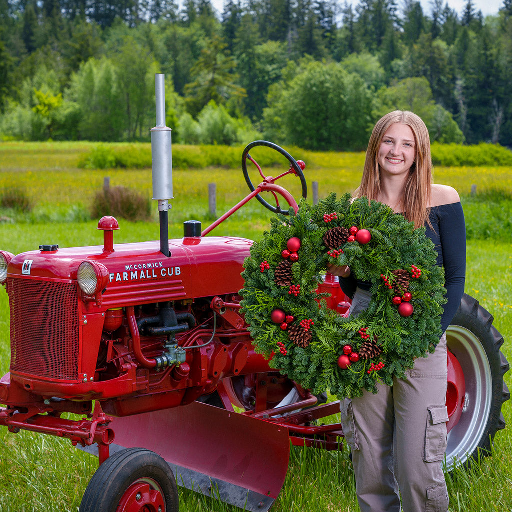 An evergreen wreath of noble fir and cedar with natural pinecones, faux red berries, and red ball ornaments