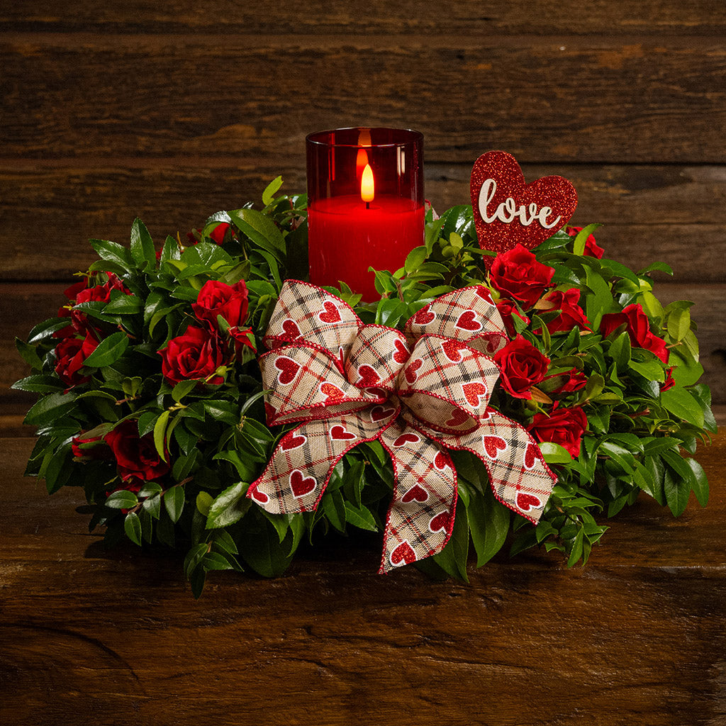 Fresh salal and green huckleberry with faux mini red roses, a red heart “love” sign, a red heart bow, and a red LED candle.