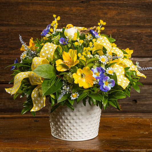 Fresh salal and green huckleberry with faux pansies, faux lavender, and faux yellow Alstromeria lilies, a yellow bird, and yellow polka-dot bows in a white metal pot