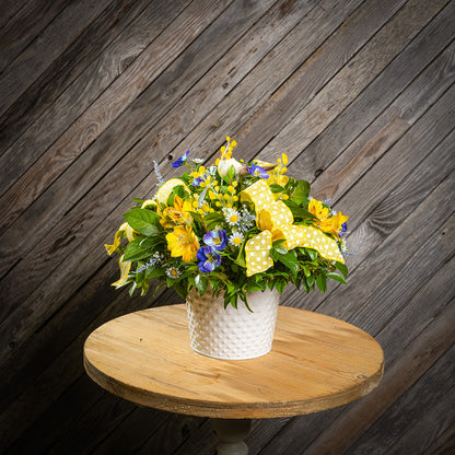 Fresh salal and green huckleberry with faux pansies, faux lavender, and faux yellow Alstromeria lilies, a yellow bird, and yellow polka-dot bows in a white metal pot