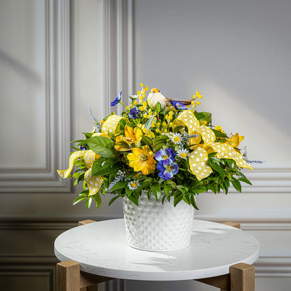 Fresh salal and green huckleberry with faux pansies, faux lavender, and faux yellow Alstromeria lilies, a yellow bird, and yellow polka-dot bows in a white metal pot