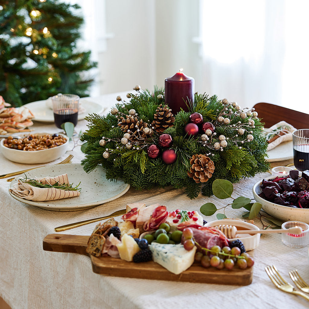 Centerpiece made of verdant fresh noble fir, white pine, and incense cedar decorated with glittery beads and shiny burgundy balls, natural pinecones and a deep burgundy pillar candle