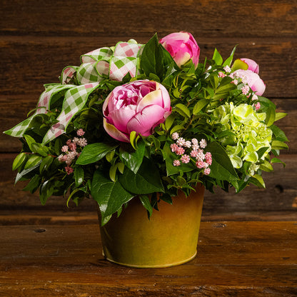 Fresh salal and green huckleberry with faux green hydrangeas, faux pink peonies, faux pink baby’s breath flowers, and plaid mauve and a sage-green bow in a spring-colored metal pot