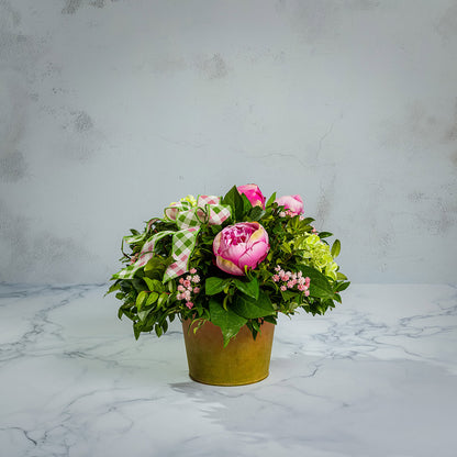 Fresh salal and green huckleberry with faux green hydrangeas, faux pink peonies, faux pink baby’s breath flowers, and plaid mauve and a sage-green bow in a spring-colored metal pot