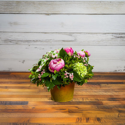 Fresh salal and green huckleberry with faux green hydrangeas, faux pink peonies, faux pink baby’s breath flowers, and plaid mauve and a sage-green bow in a spring-colored metal pot