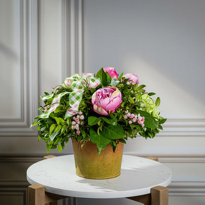 Fresh salal and green huckleberry with faux green hydrangeas, faux pink peonies, faux pink baby’s breath flowers, and plaid mauve and a sage-green bow in a spring-colored metal pot