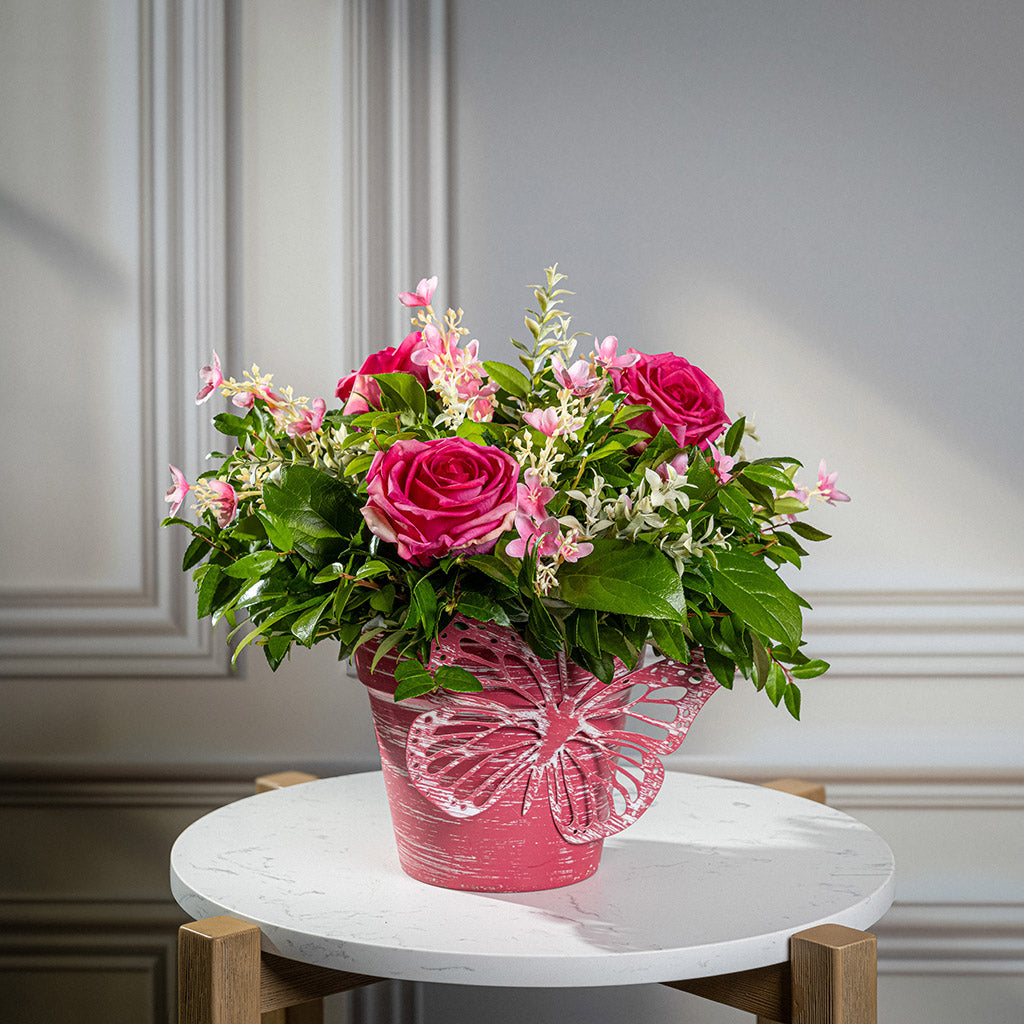 Fresh salal and green huckleberry with faux pink roses and faux pink wildflowers in a pink butterfly-themed metal pot