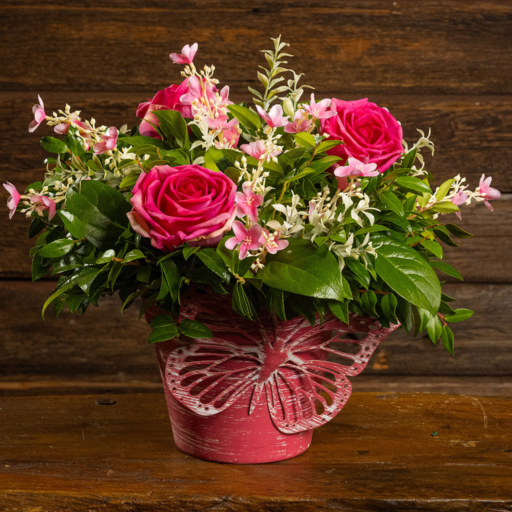 Fresh salal and green huckleberry with faux pink roses and faux pink wildflowers in a pink butterfly-themed metal pot