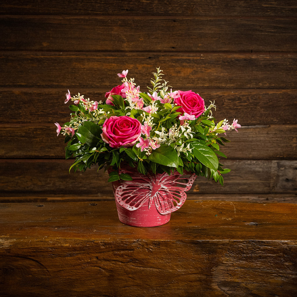 Fresh salal and green huckleberry with faux pink roses and faux pink wildflowers in a pink butterfly-themed metal pot