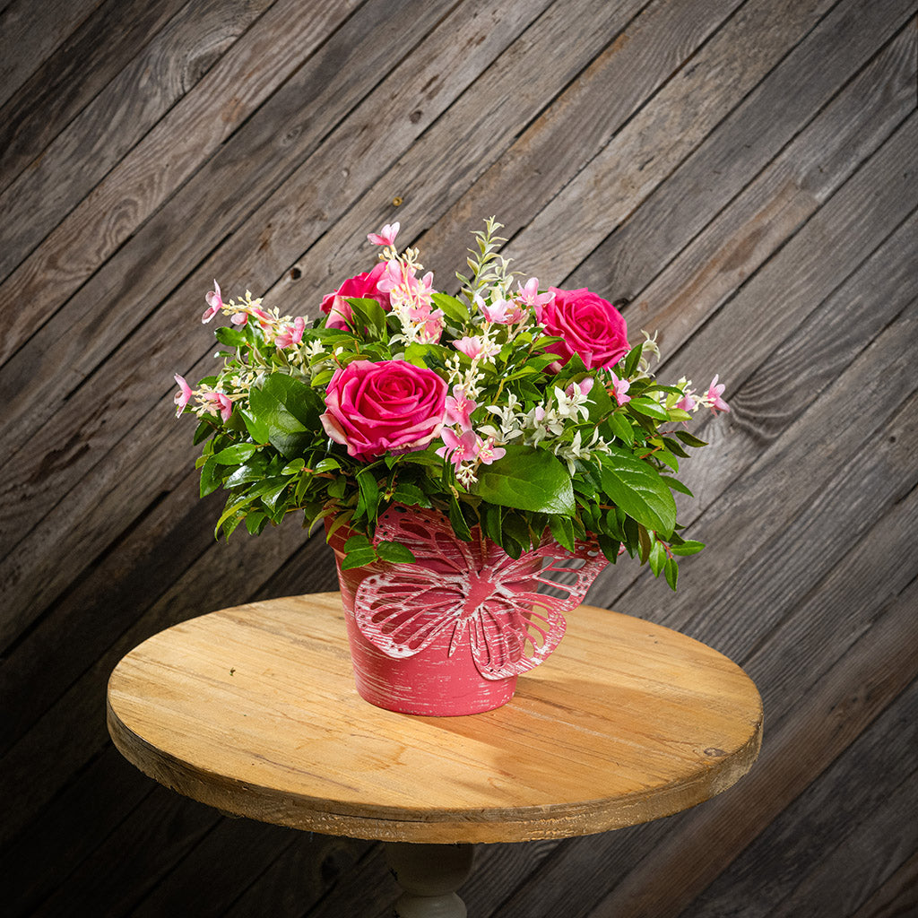 Fresh salal and green huckleberry with faux pink roses and faux pink wildflowers in a pink butterfly-themed metal pot