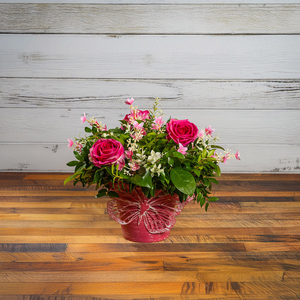 Fresh salal and green huckleberry with faux pink roses and faux pink wildflowers in a pink butterfly-themed metal pot