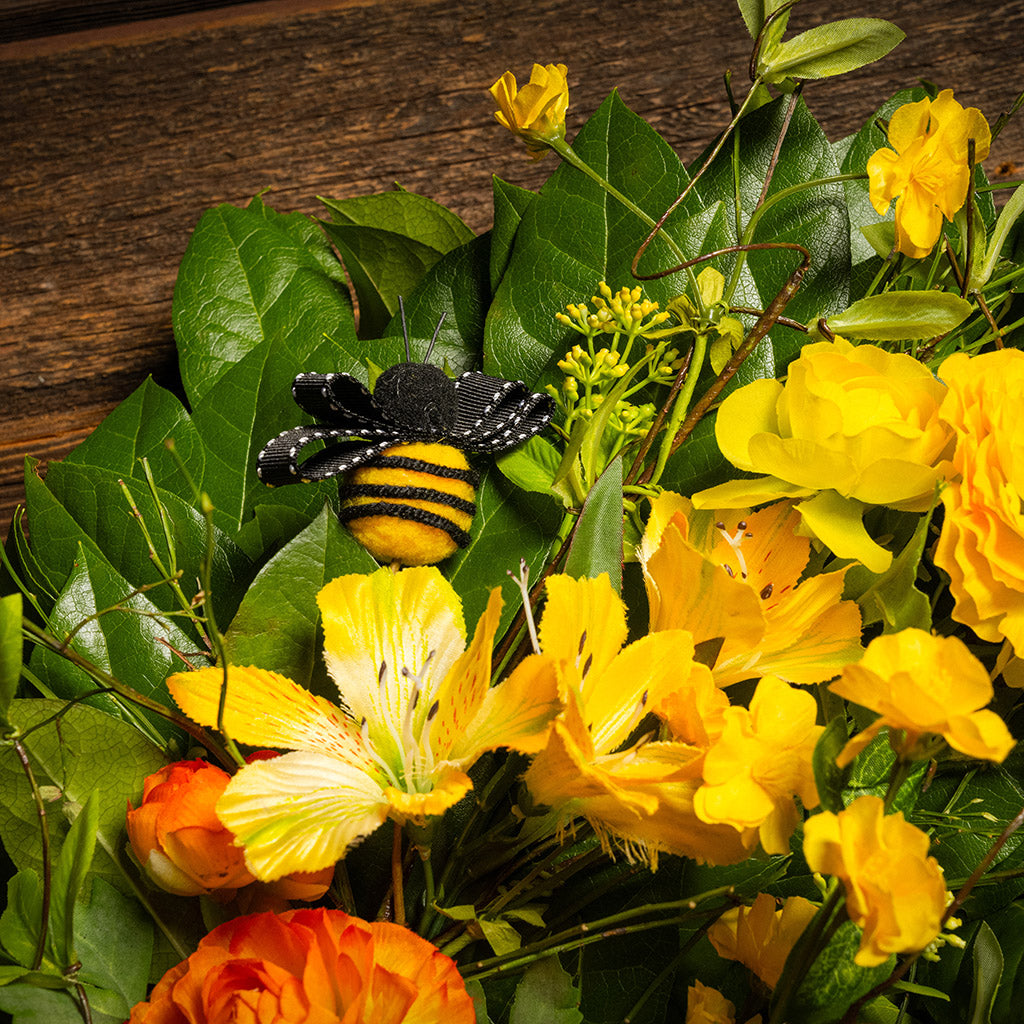 Fresh salal and sweet huckleberry with faux spring wildflowers, faux gerbera daisies, faux yellow and orange ranunculus flowers, honey bees