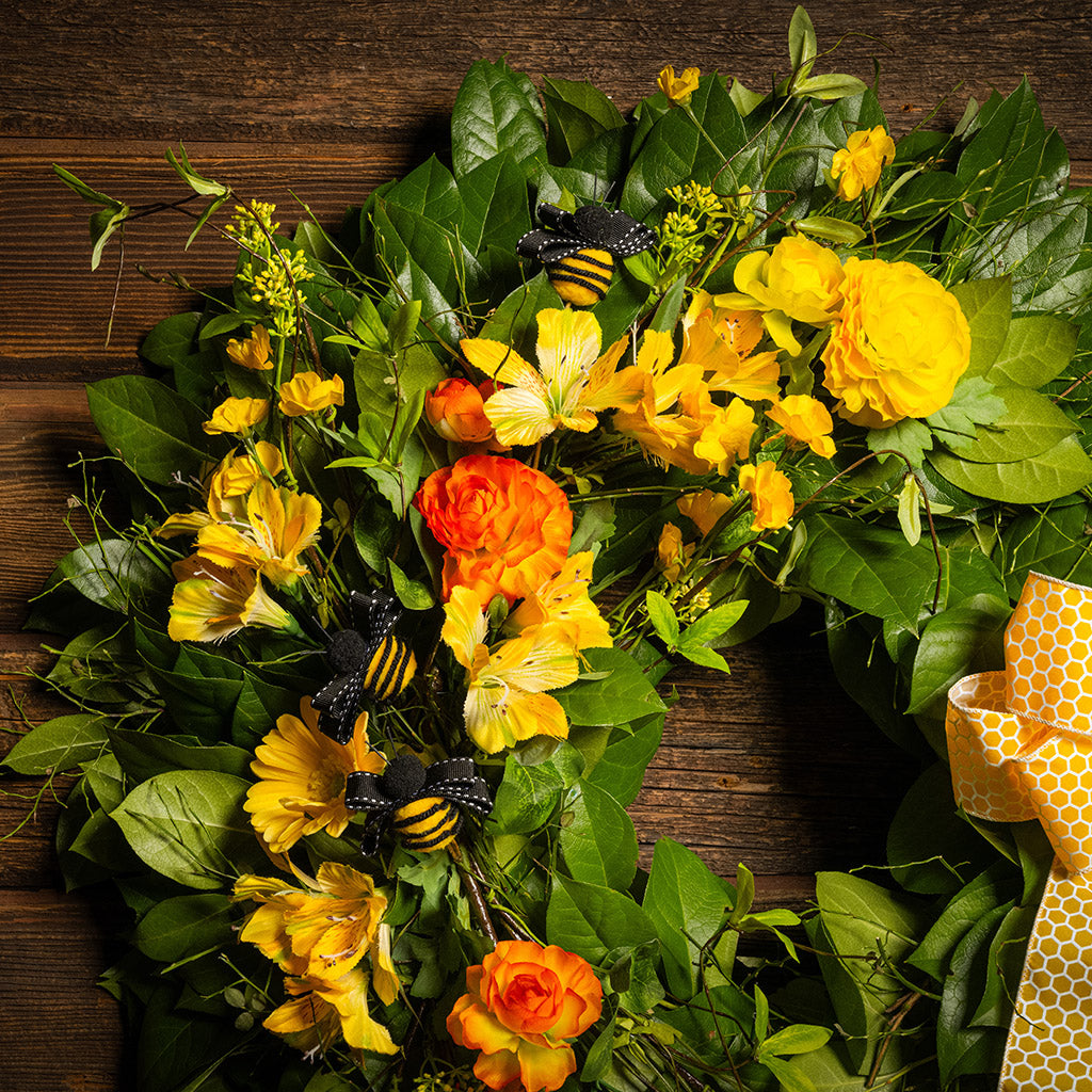 Fresh salal and sweet huckleberry with faux spring wildflowers, faux gerbera daisies, faux yellow and orange ranunculus flowers, honey bees, and a yellow honeycomb-patterned bow