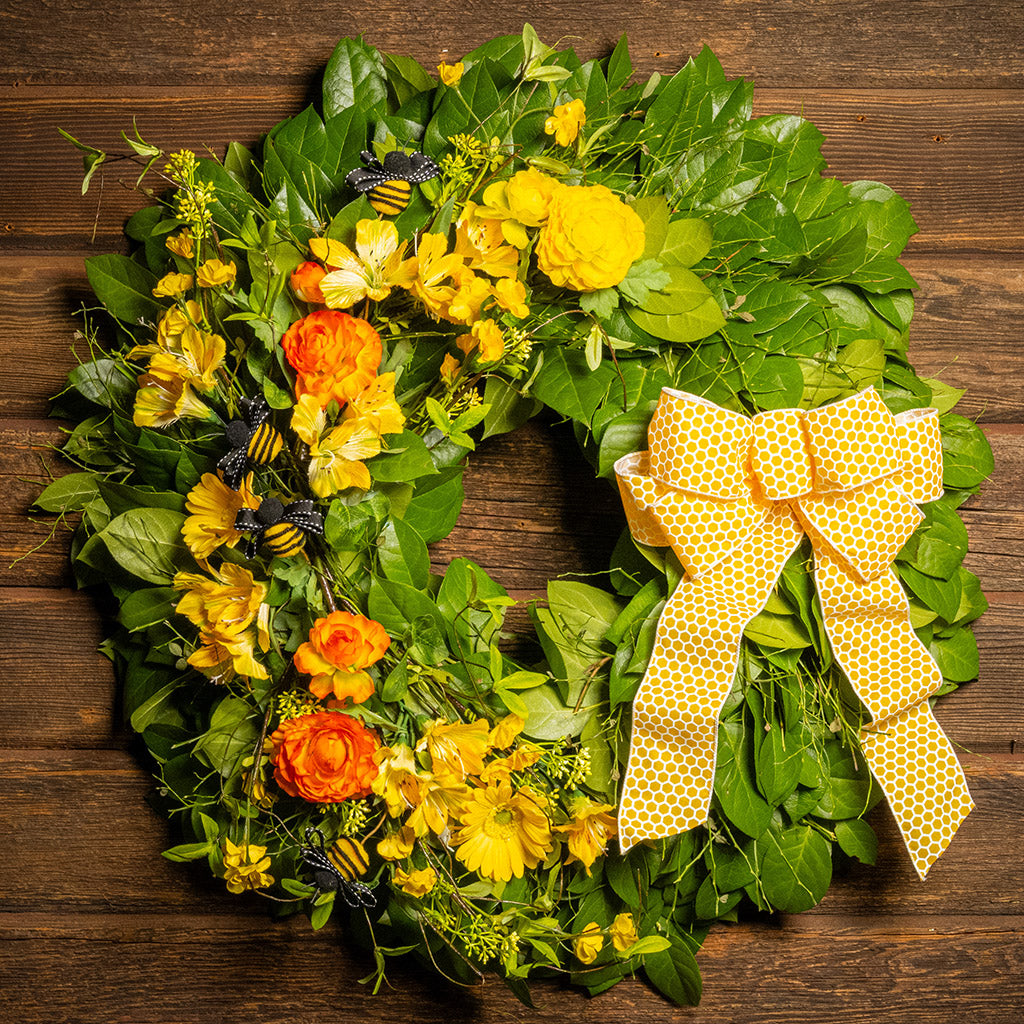 Fresh salal and sweet huckleberry with faux spring wildflowers, faux gerbera daisies, faux yellow and orange ranunculus flowers, honey bees, and a yellow honeycomb-patterned bow