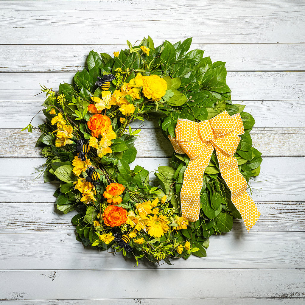 Fresh salal and sweet huckleberry with faux spring wildflowers, faux gerbera daisies, faux yellow and orange ranunculus flowers, honey bees, and a yellow honeycomb-patterned bow