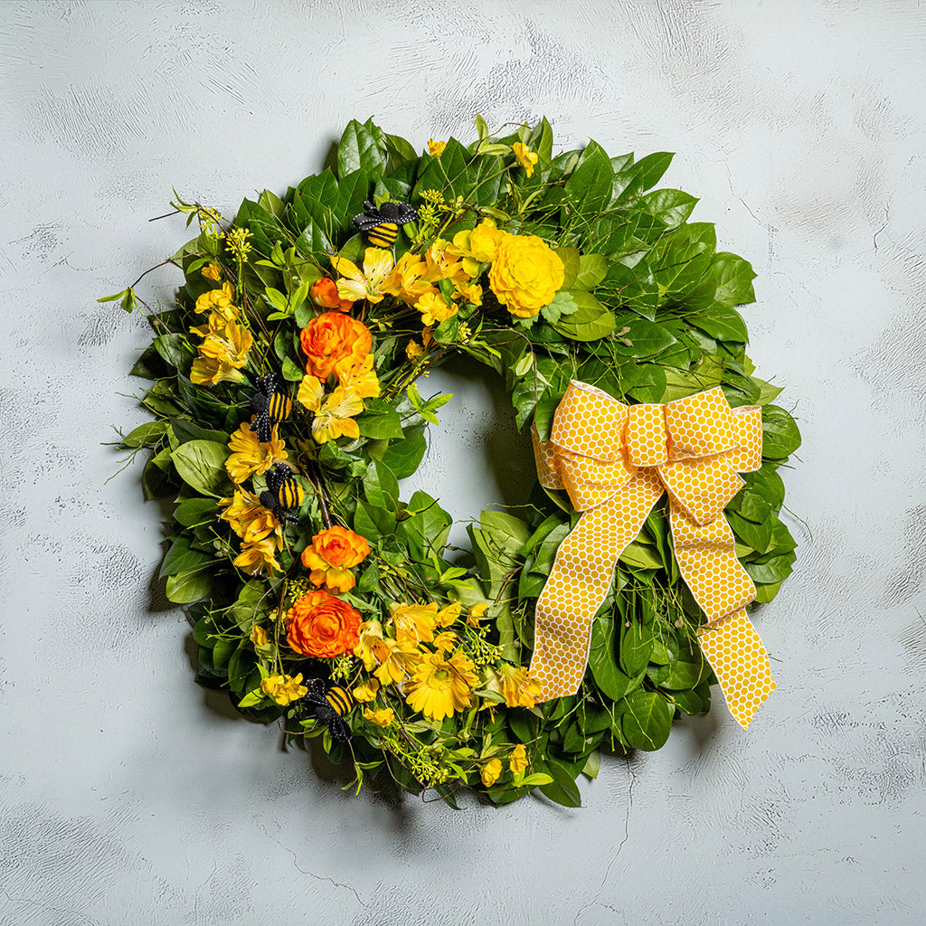 Fresh salal and sweet huckleberry with faux spring wildflowers, faux gerbera daisies, faux yellow and orange ranunculus flowers, honey bees, and a yellow honeycomb-patterned bow