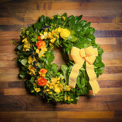 Fresh salal and sweet huckleberry with faux spring wildflowers, faux gerbera daisies, faux yellow and orange ranunculus flowers, honey bees, and a yellow honeycomb-patterned bow