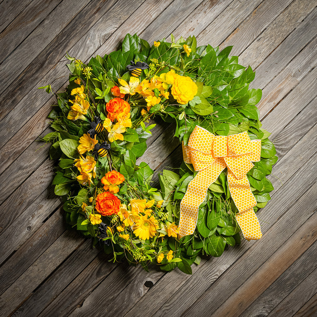 Fresh salal and sweet huckleberry with faux spring wildflowers, faux gerbera daisies, faux yellow and orange ranunculus flowers, honey bees, and a yellow honeycomb-patterned bow