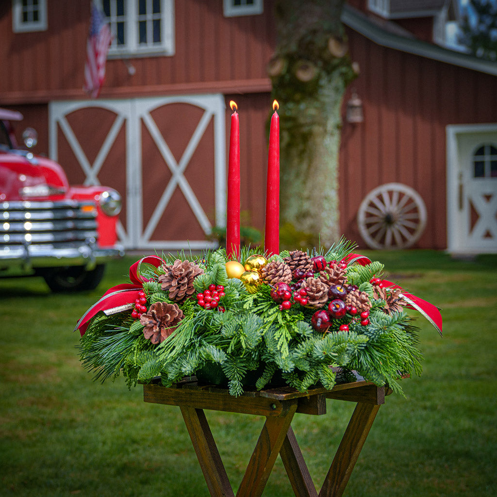 Traditional centerpiece with red balls, pine cones and berries with 2 red velveteen bows and two red taper candles