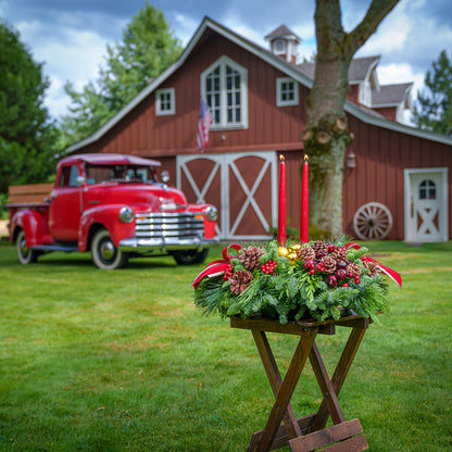 Traditional centerpiece with red balls, pine cones and berries with 2 red velveteen bows and two red taper candles