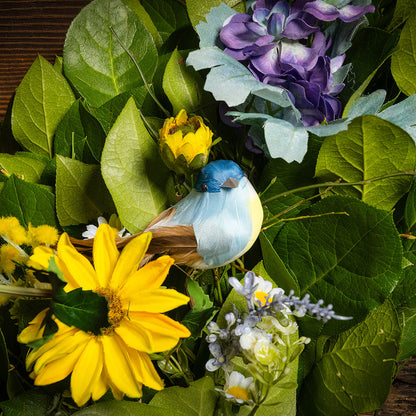 Fresh salal and sweet huckleberry with faux lavender pansies, faux yellow forsythia flowers, faux purple delphinium flowers, faux yellow daisies, and three birds with a yellow polka-dot bow